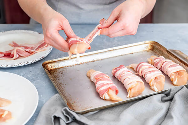 Wrapping chicken with bacon.