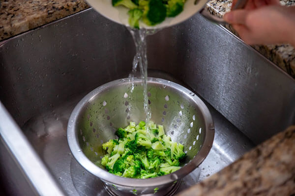 Broccoli being strained out in a colander.